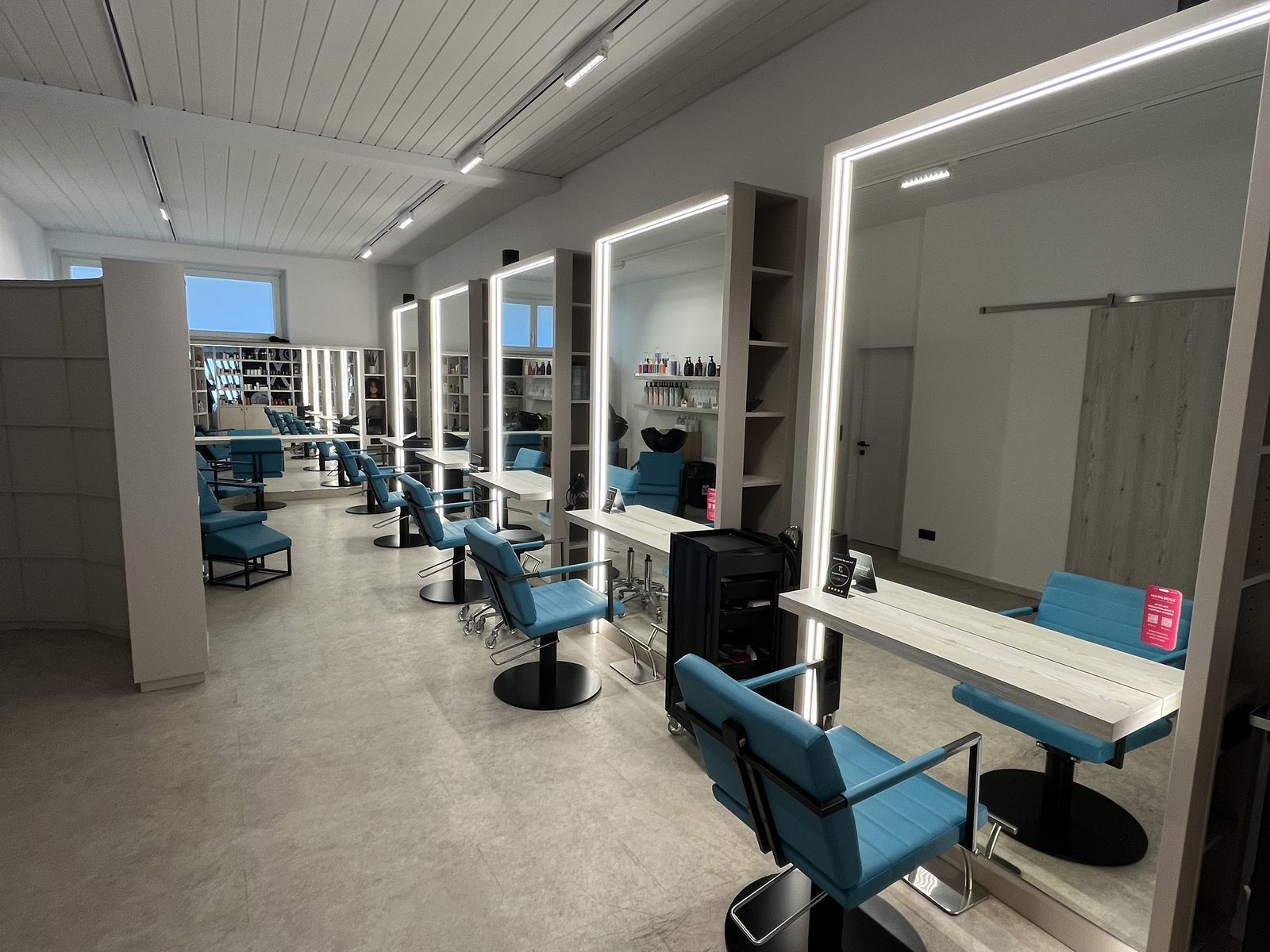 View along the HAIRLODGE Ellmau salon: teal styling chairs lined up in front of the illuminated mirrors along the bright wall.