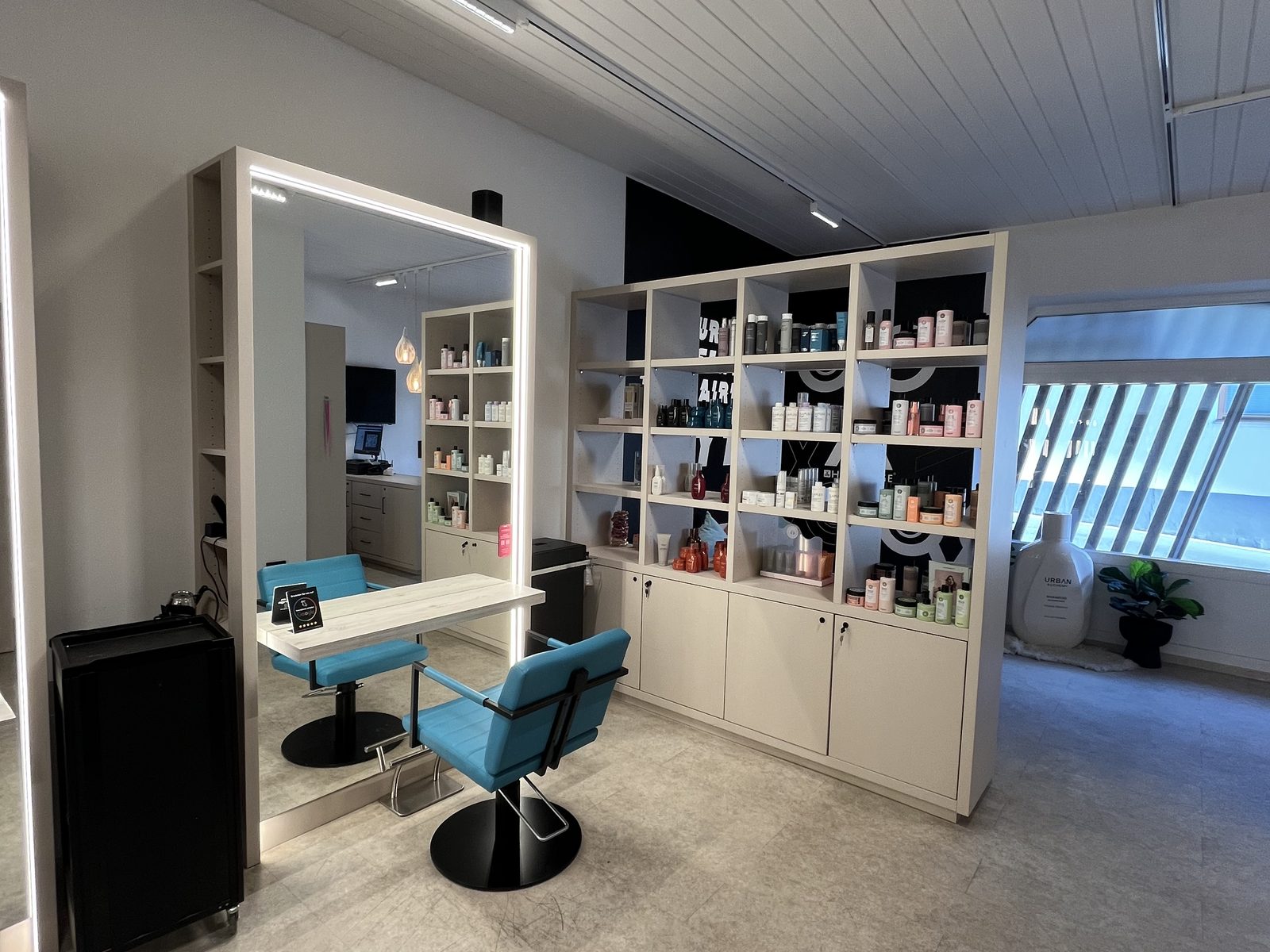 A single styling station at HAIRLODGE Ellmau next to a large shelf of hair-care products, with daylight coming in from the window.