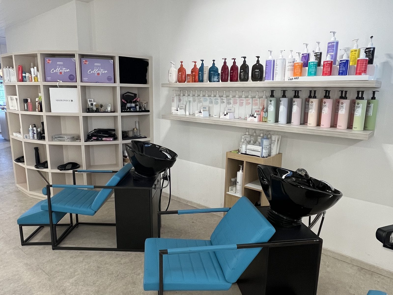 Wash area at HAIRLODGE Ellmau with teal wash loungers and a shelf full of colour and care products.