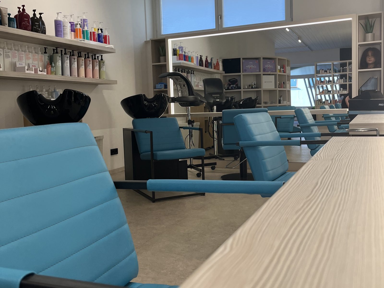 Styling stations at HAIRLODGE Ellmau: teal chairs at the pale wooden counter in front of the illuminated mirrors.