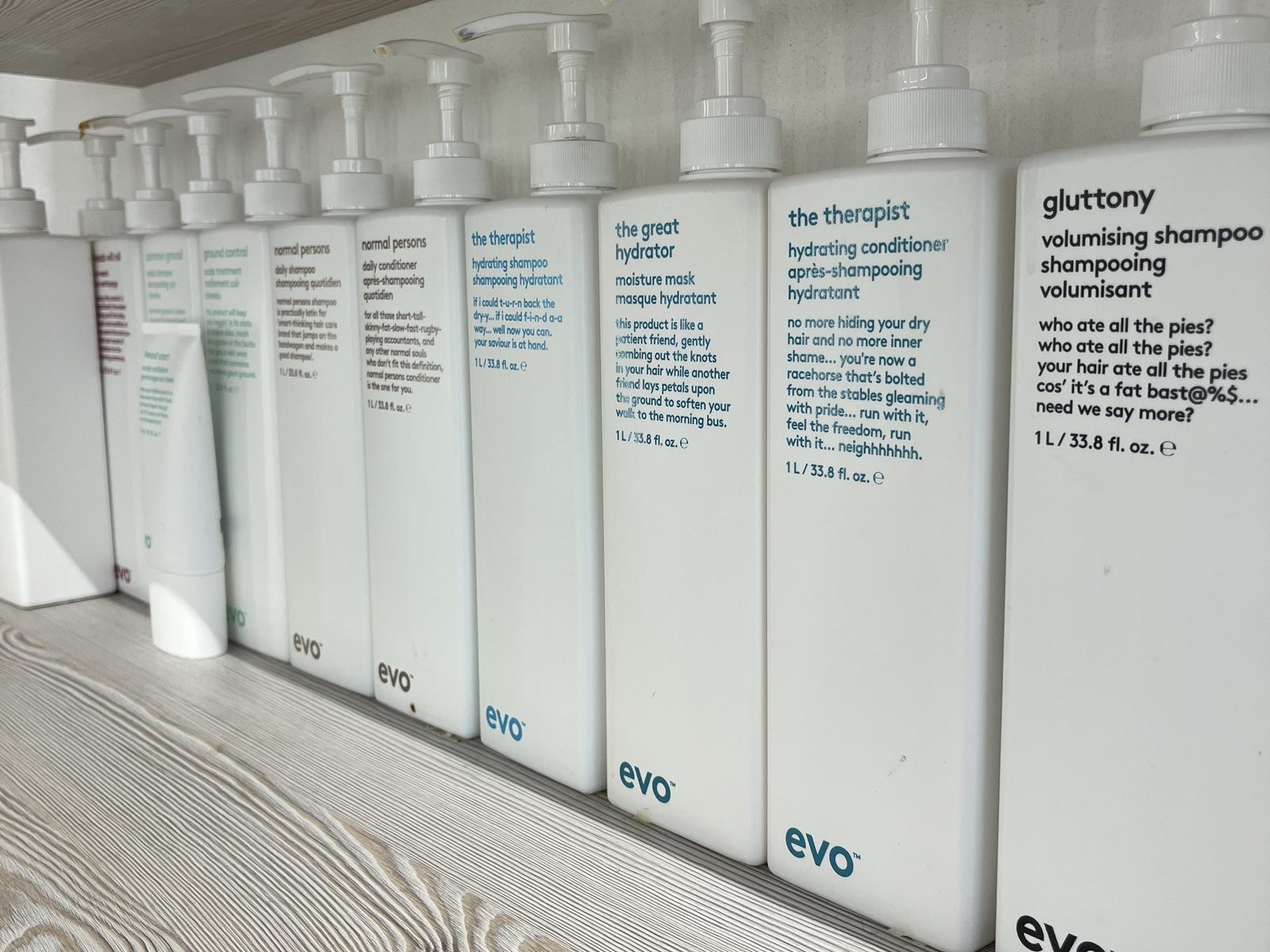 The evo care range in large one-litre bottles on the wooden shelf at HAIRLODGE Ellmau.
