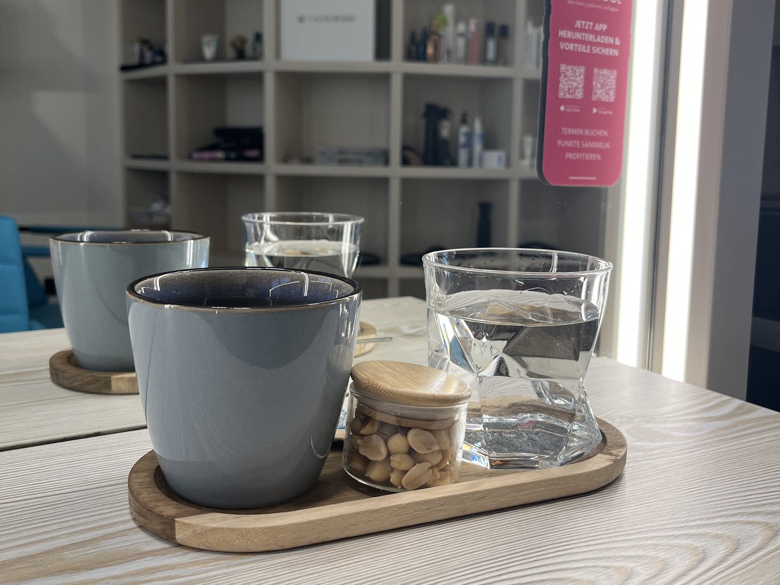 Coffee and water served on a wooden tray at HAIRLODGE Ellmau, with the HAIRLODGE app promotion in the background.