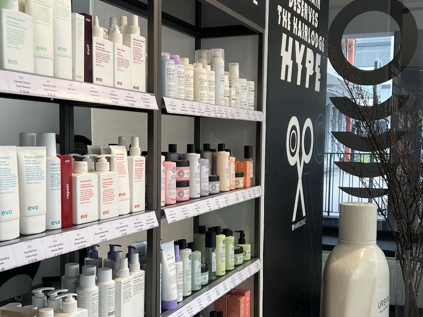 Product wall at HAIRLODGE Kufstein stocked with evo, Olaplex, Maria Nila and Urban Alchemy, beside the slogan "Your hair deserves the HAIRLODGE hype".