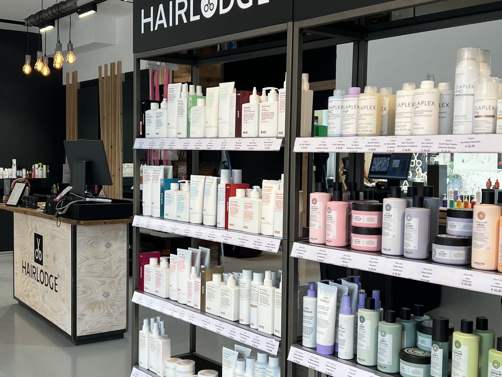 Retail shelves stocked with evo, Olaplex and Maria Nila under the HAIRLODGE signs, with the reception desk behind, at HAIRLODGE Kufstein.