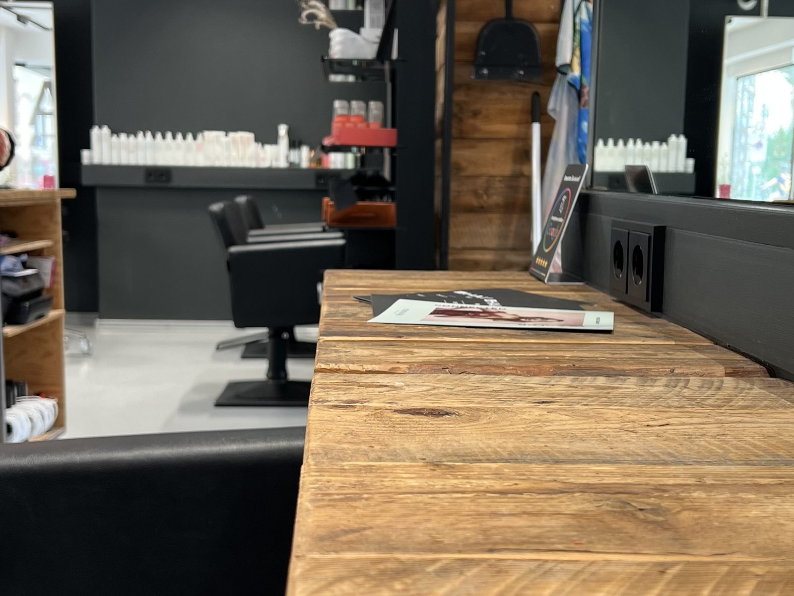 Solid reclaimed-wood counter at HAIRLODGE Kufstein, with the dark styling stations and mirrors behind.