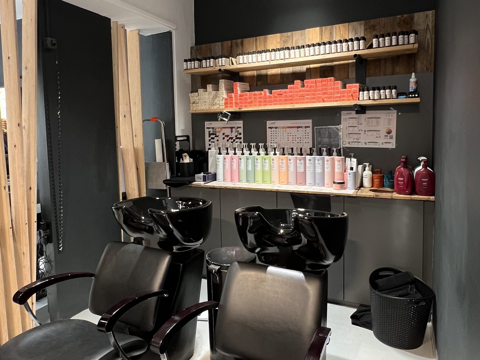 Wash room at HAIRLODGE Kufstein with two wash stations, the colour shelf and the wooden slat wall leading through to the salon.