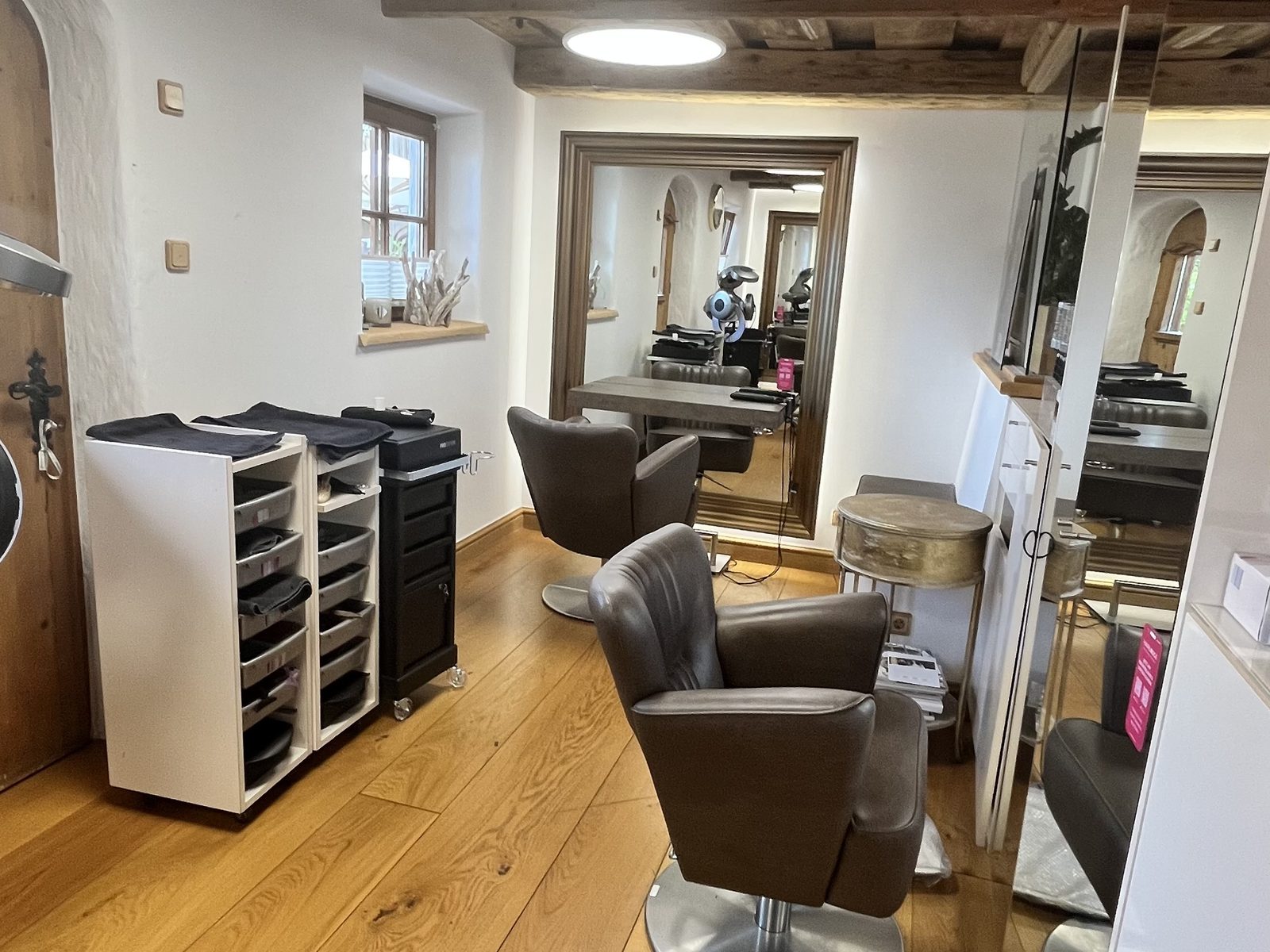 Salon room at HAIRLODGE Stanglwirt beneath the old beamed ceiling, with styling chairs and work trolleys.