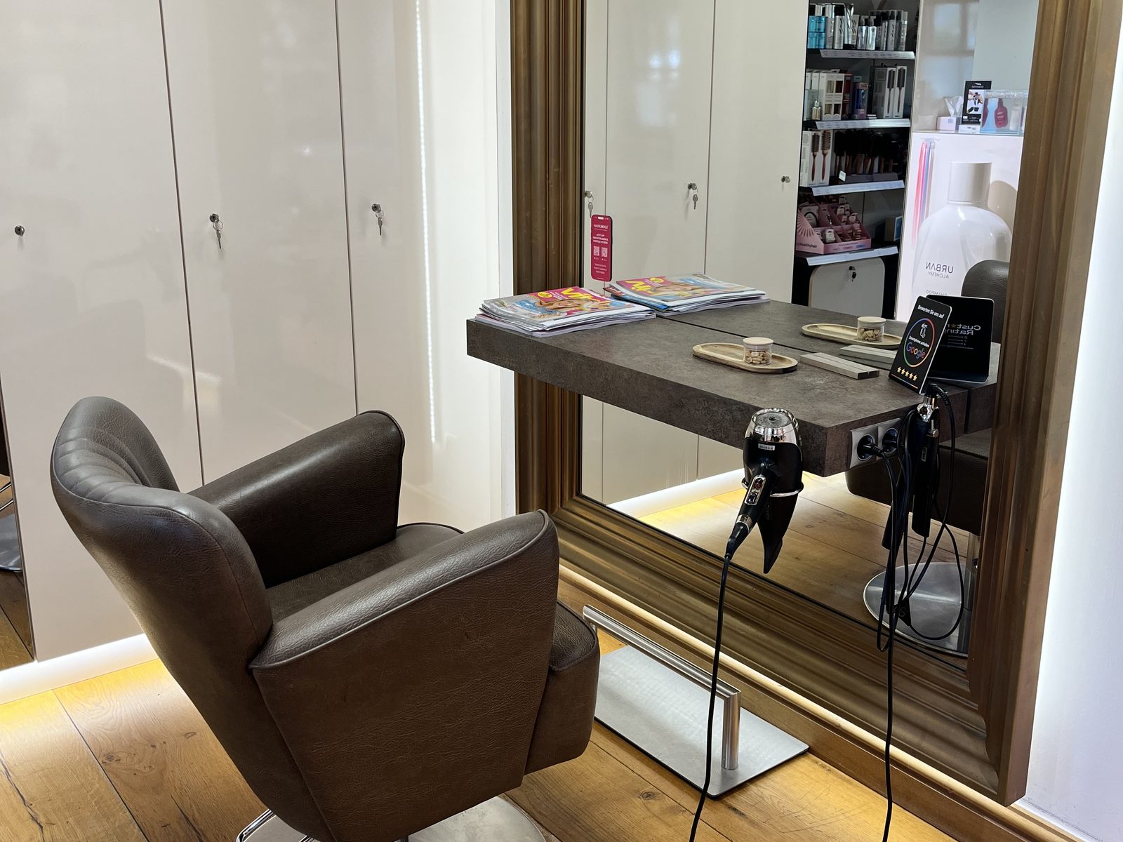 Styling station at HAIRLODGE Stanglwirt with a gold-framed mirror, brown leather chair and console on oak floorboards.